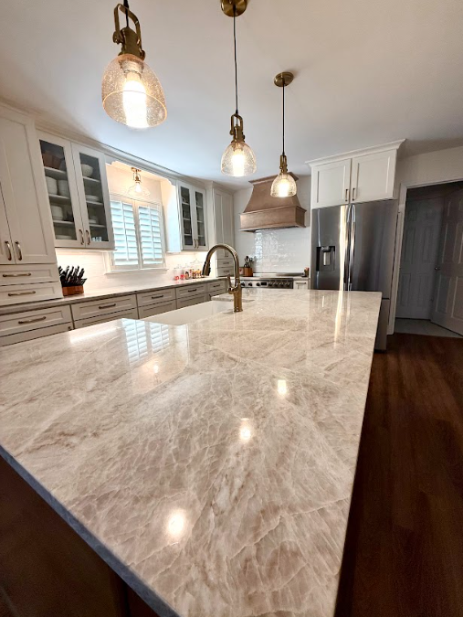 Modern kitchen with a marble island, hanging pendant lights, white cabinets, and a stainless-steel refrigerator