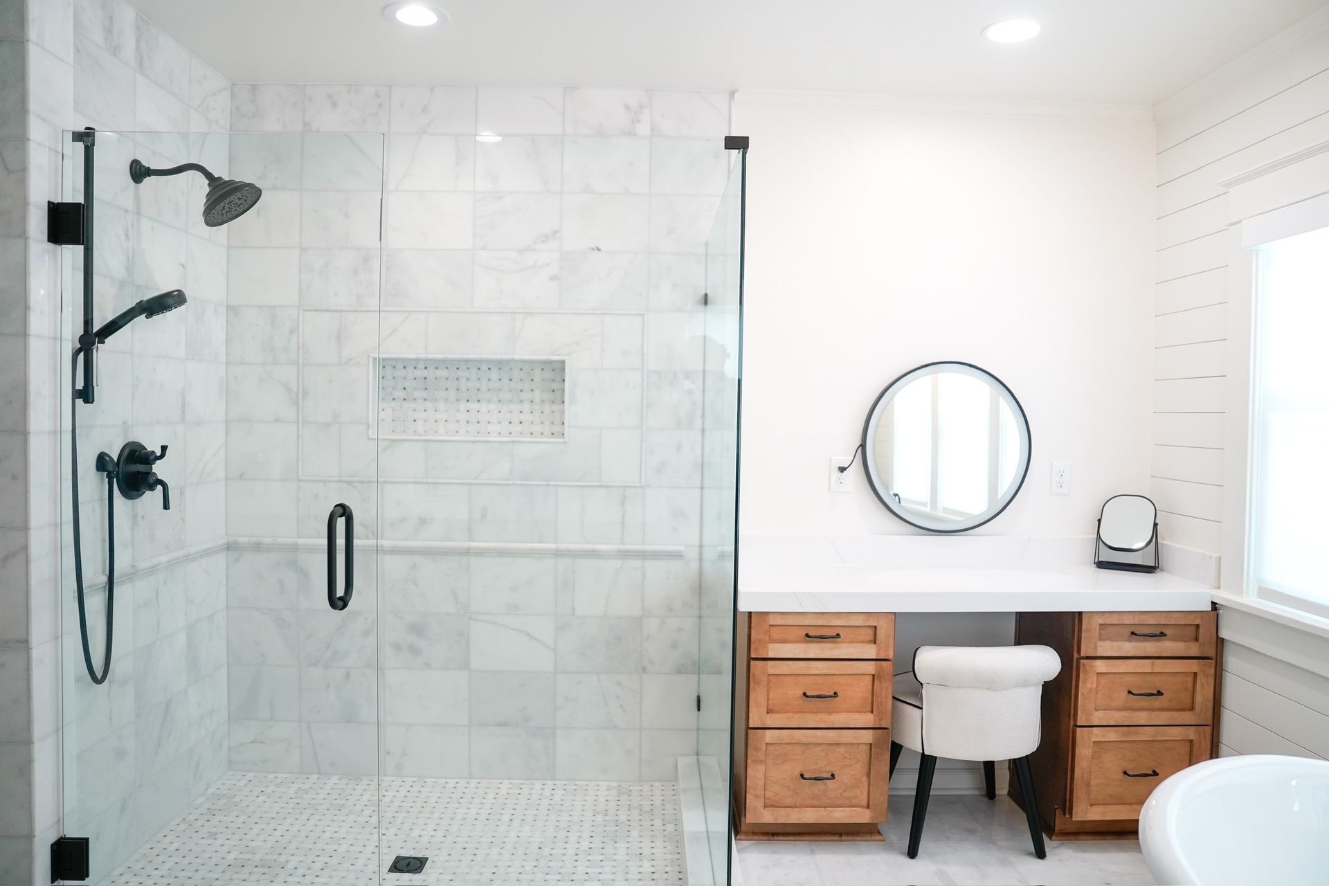 Modern white bathroom with glass shower, wood vanity, round mirror, and white toilet