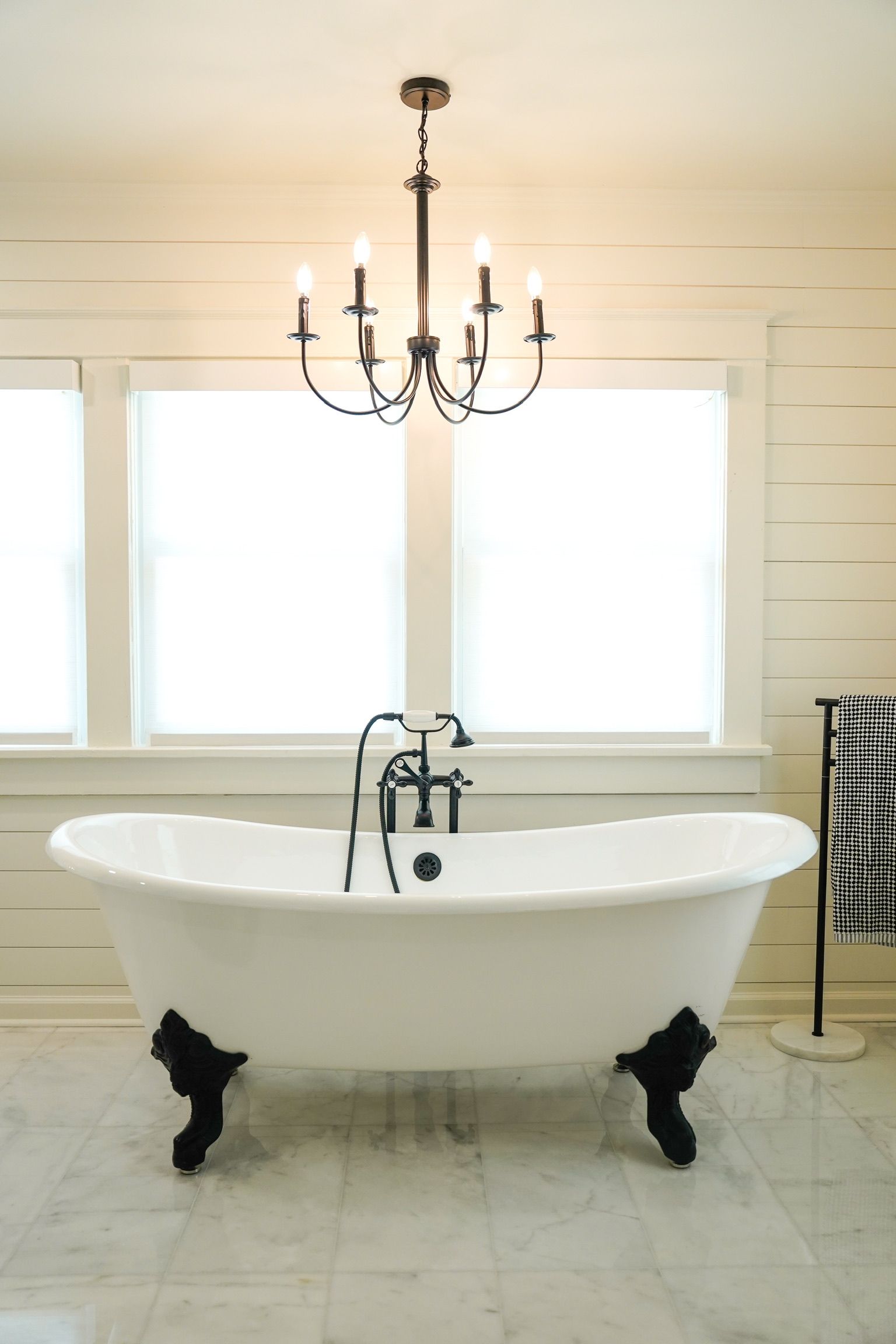 Freestanding white bathtub beneath a black chandelier in a bright, modern bathroom