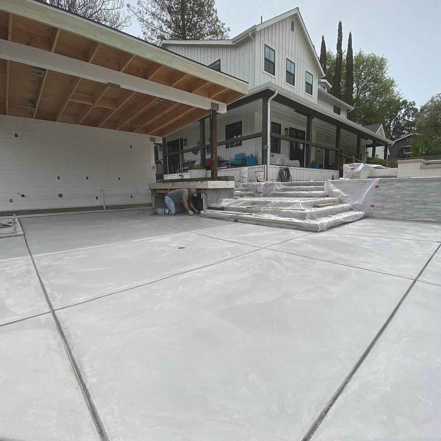 A new concrete driveway leads to a modern farmhouse with a porch and steps under construction.