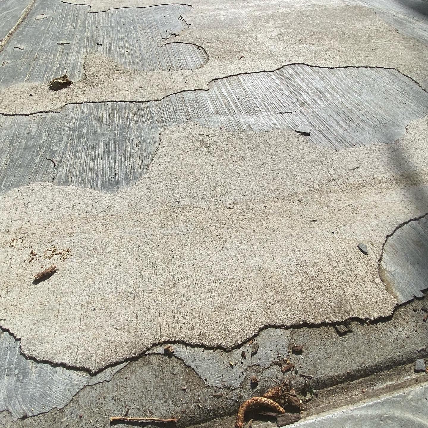 Large sections of light-colored concrete have flaked and peeled off, revealing a rougher, darker gray surface underneath.