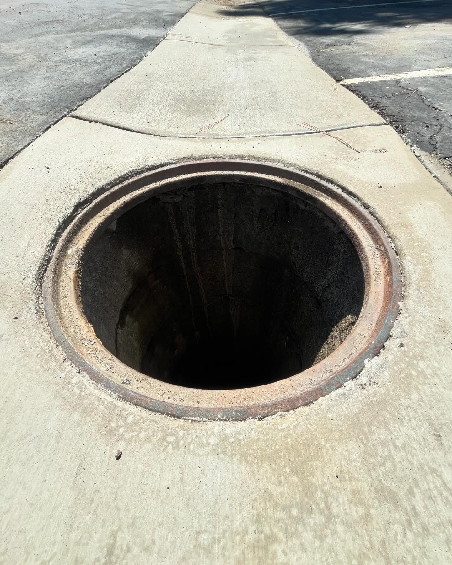 An open manhole in the middle of a concrete sidewalk.