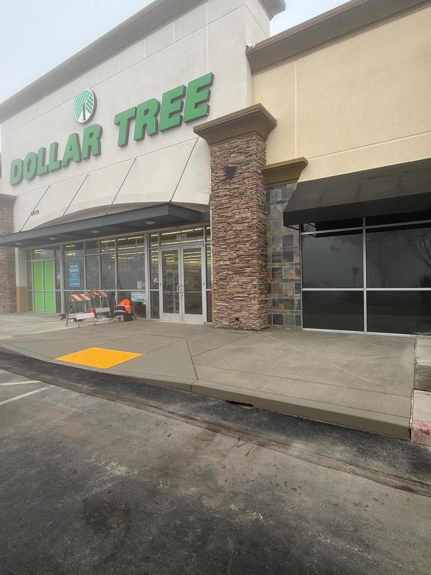 A Dollar Tree store entrance with a beige facade, a stone pillar, a black awning, and a concrete ramp in front.