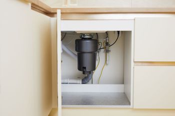 Open cabinet under sink showing garbage disposal and plumbing pipes