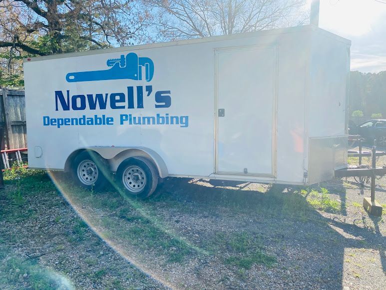 White Nowell’s Dependable Plumbing trailer parked outdoors on grass, with blue logo and text.