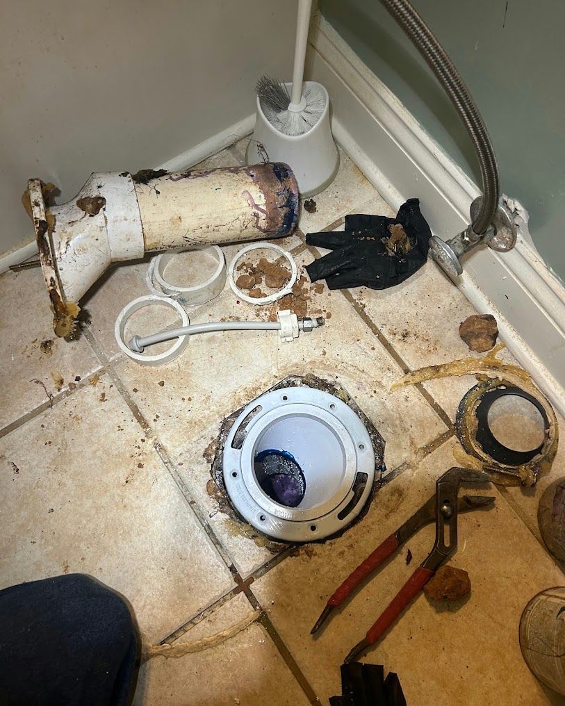 Broken toilet parts and tools scattered on a dirty bathroom floor near a drain.
