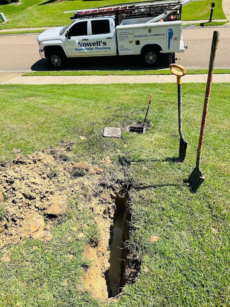 Deep trench cut in a grassy yard near utility equipment, with a work truck parked on the street.