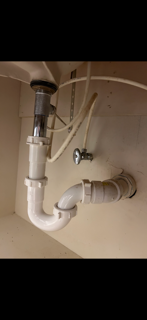 Under-sink white PVC drain pipes with a P-trap and vertical connector in a beige cabinet