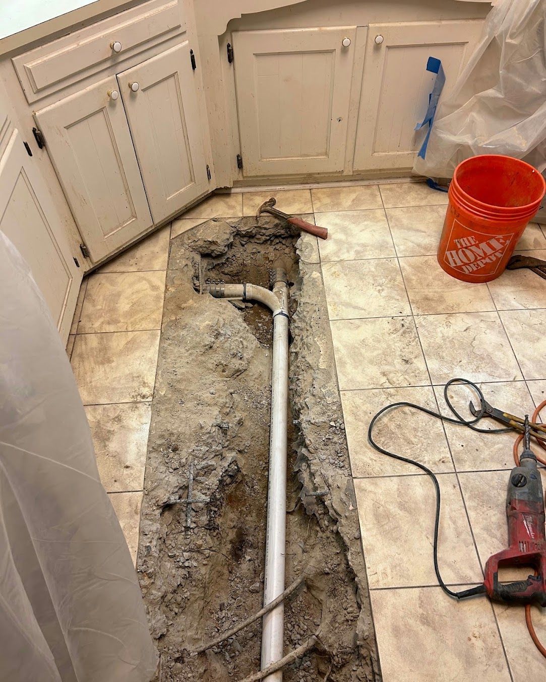 Bathroom floor torn open around a pipe, with tools and debris during repair work.
