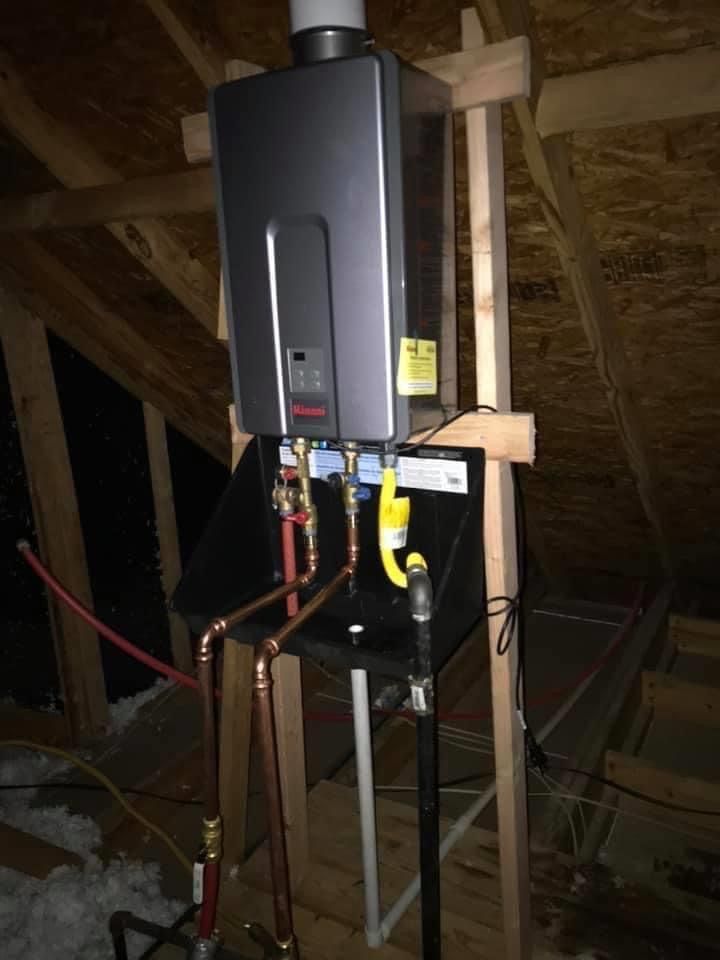 Black water heater mounted in an unfinished attic with exposed pipes and framing.