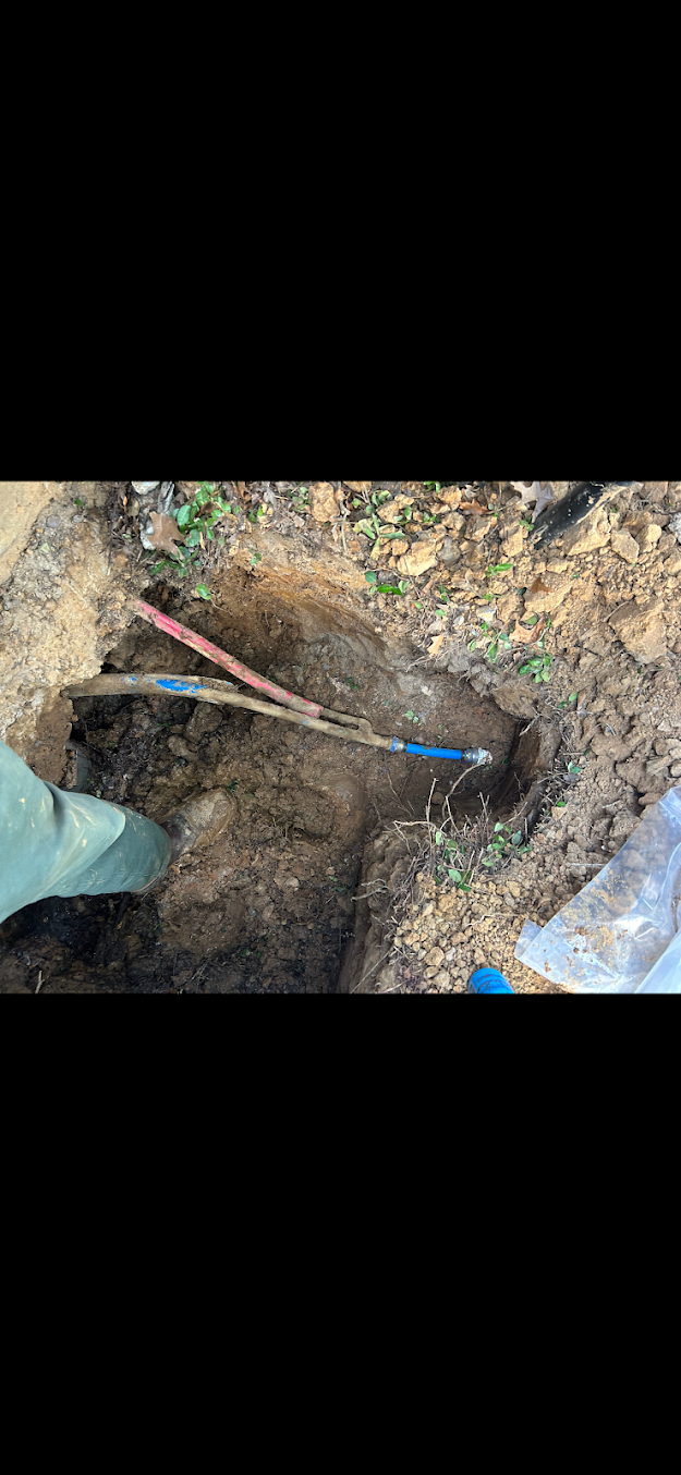 Person using a shovel to dig a hole in muddy ground beside a pipe and cables