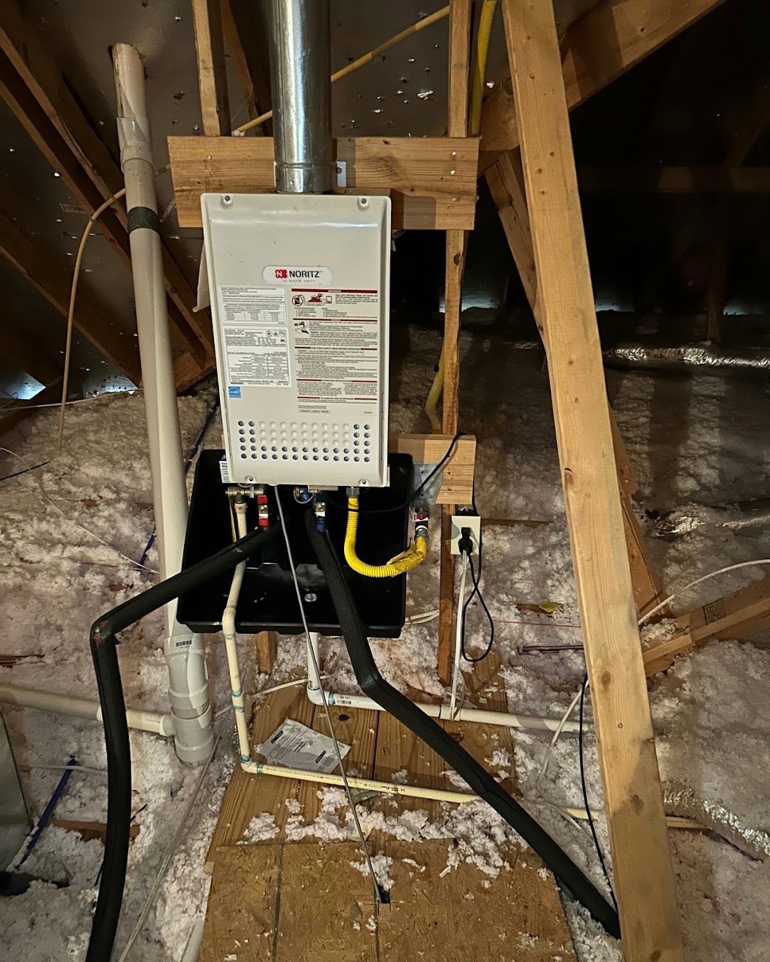 White furnace unit in an unfinished attic with exposed wooden beams and ducting.