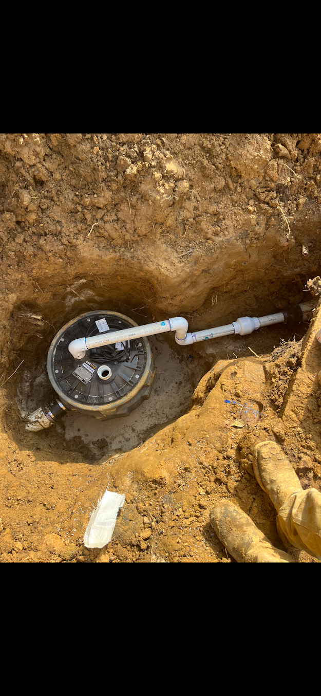 Black wheel valve in a dirt trench with a white pipe extending to the right.