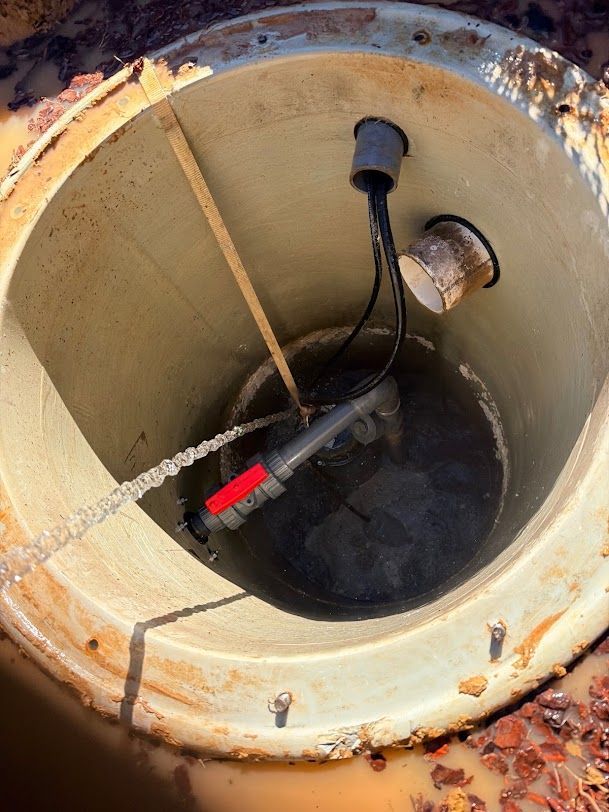 Open utility access pit with submerged pump and cables inside a rusted concrete chamber