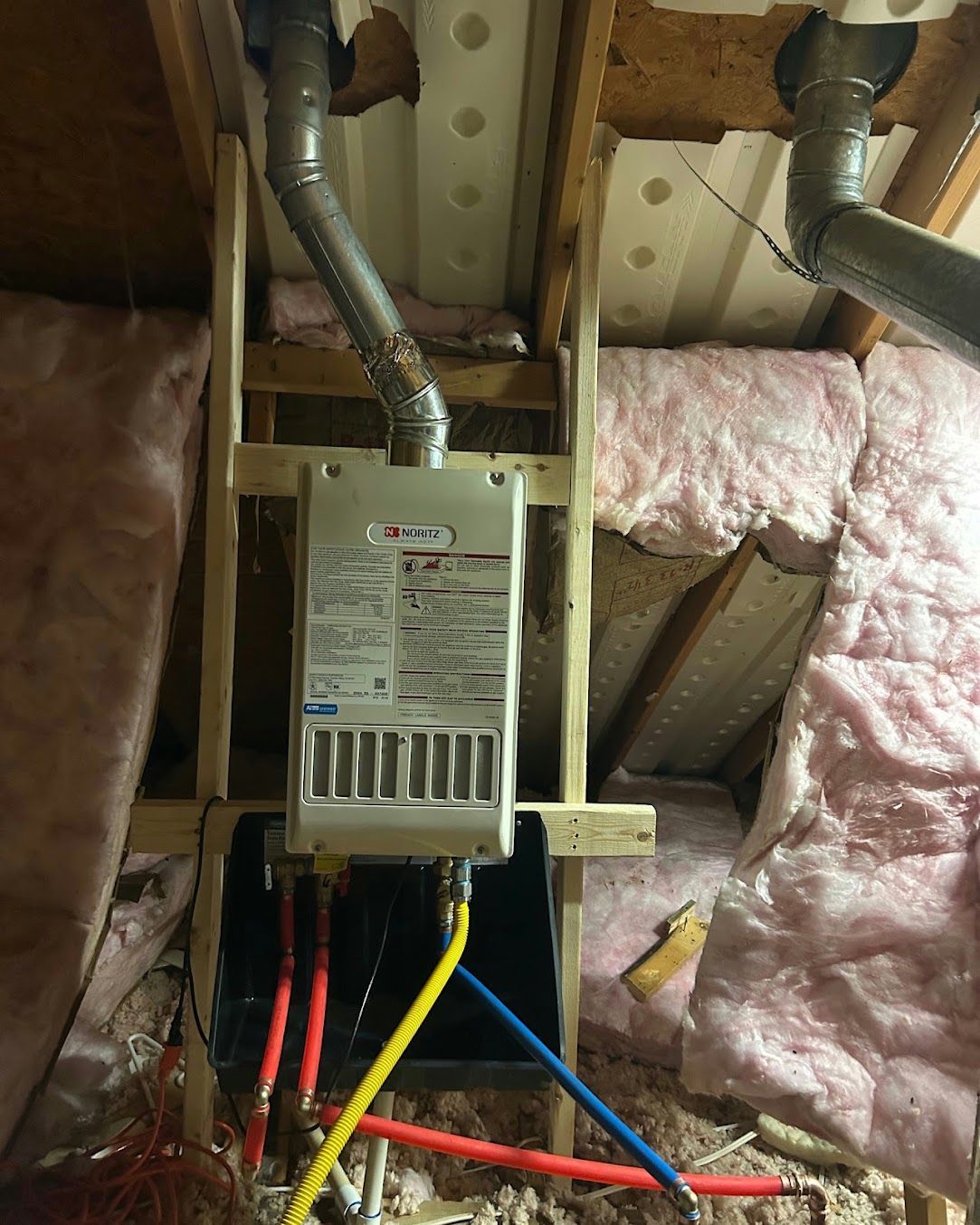 Basement furnace with exposed ducts, wiring, and pink insulation around unfinished framing.
