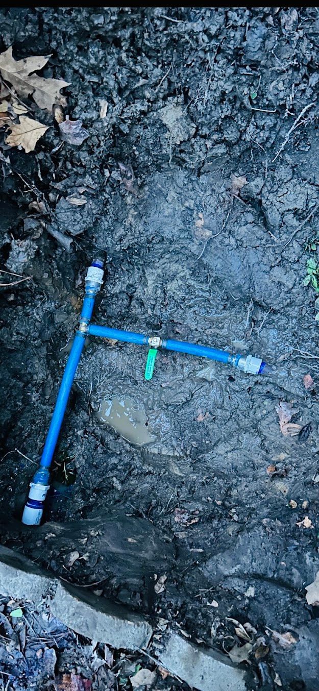 Blue survey marker on muddy ground with a small green flag and surrounding excavation soil