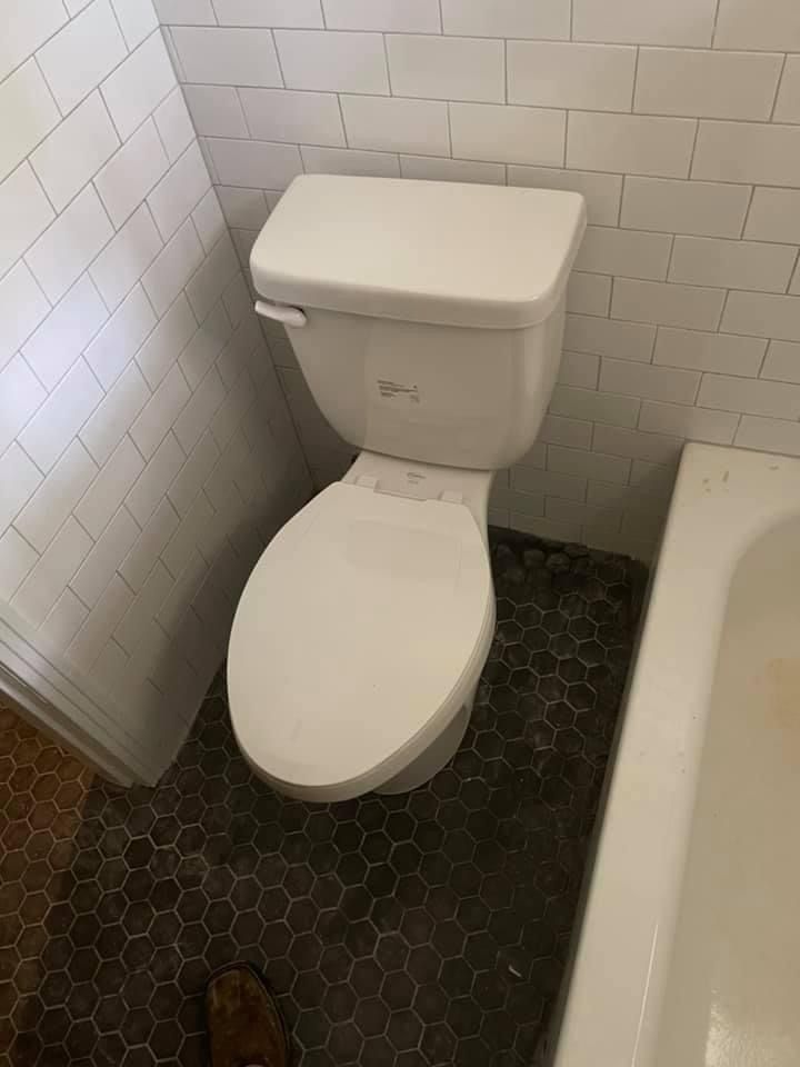 Small bathroom with a white toilet beside a bathtub and tiled walls.