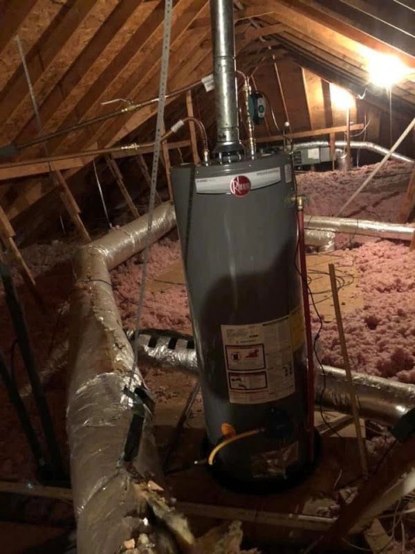 Attic utility space with a gray water heater, exposed ducts, and pink insulation under a sloped roof.