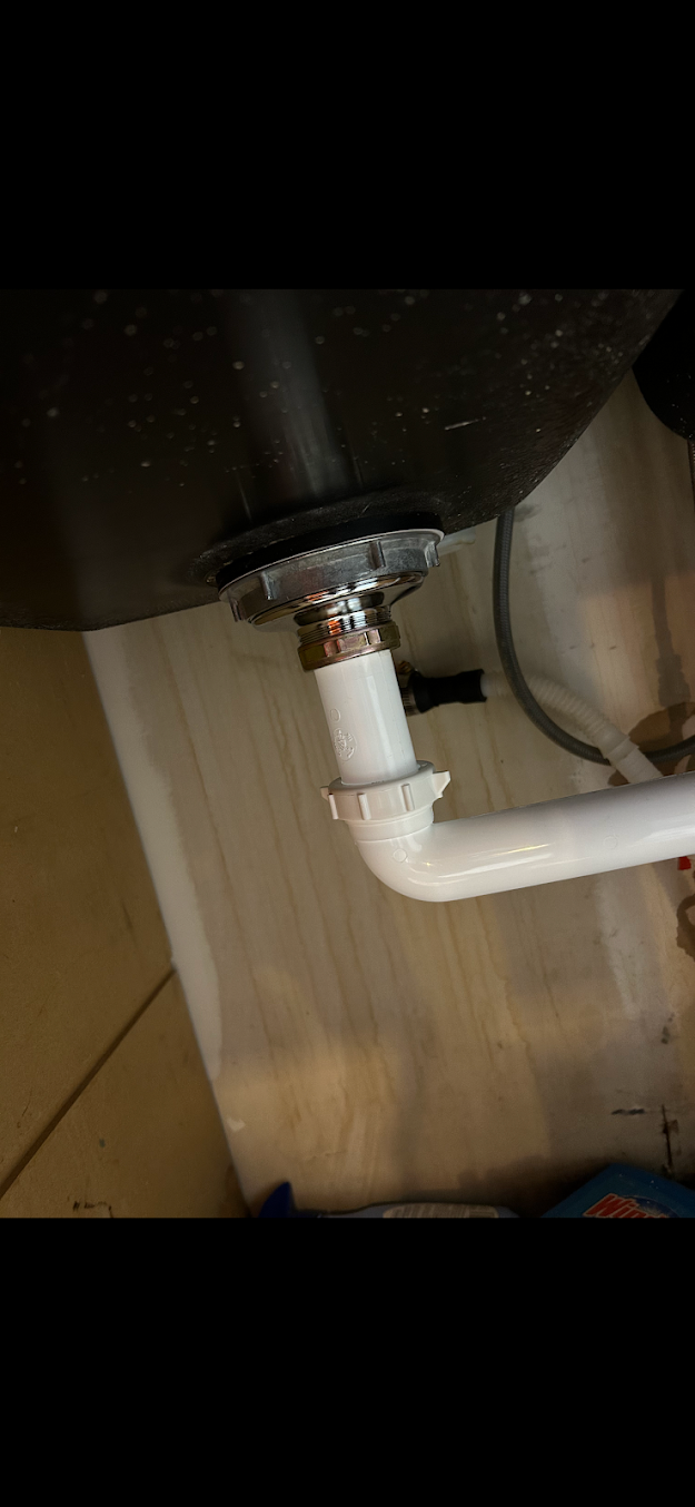 White pipe connected to a dark sink drain under a cabinet, with a metal clamp and black seal.