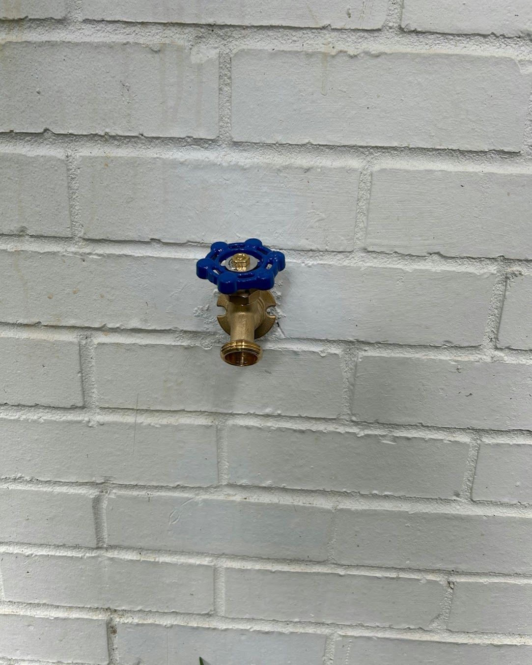 Blue water valve mounted on a white brick wall.