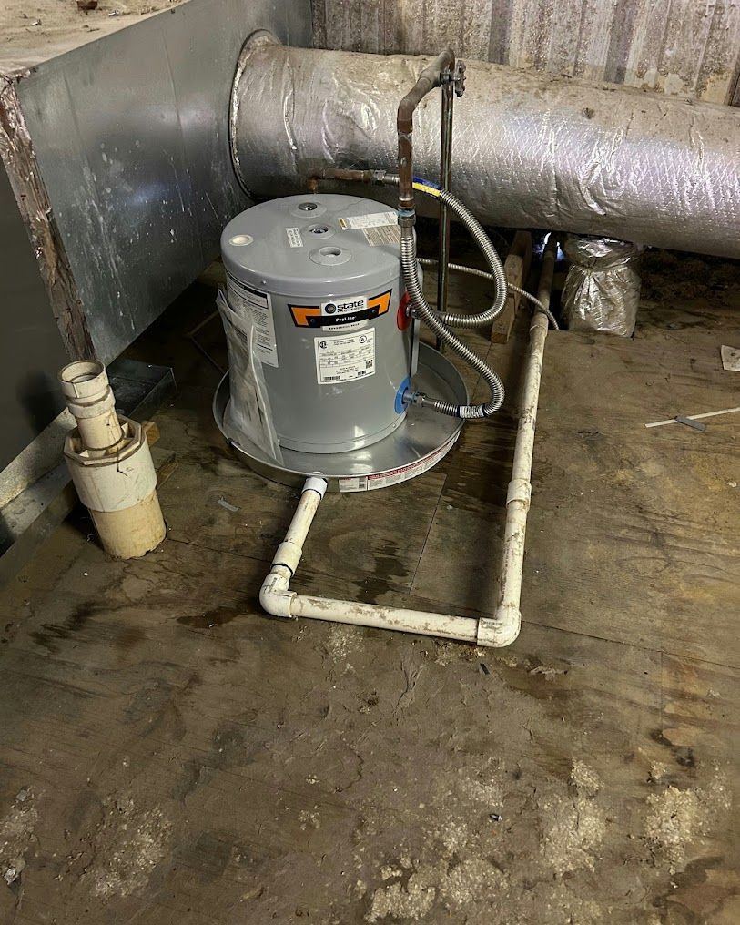Gray water heater with PVC piping in a basement utility area, beside large insulated ducts and a floor drain.