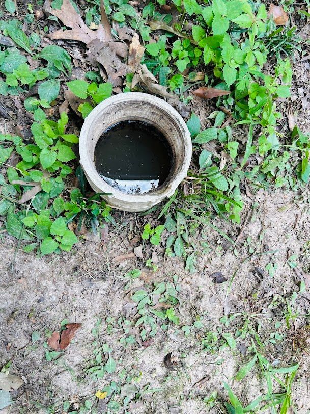 Open concrete pipe or drain hole in grassy ground with standing dark water inside