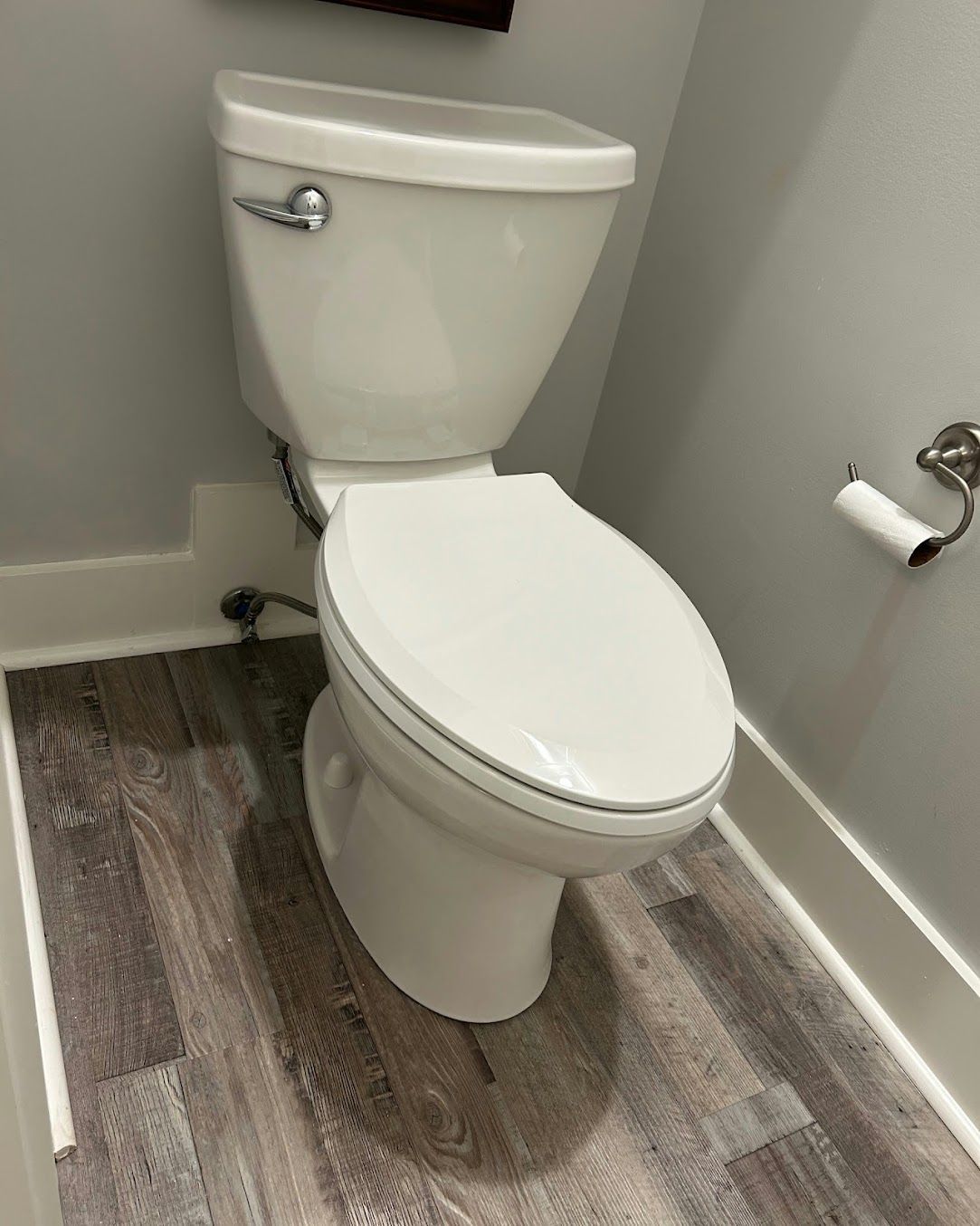 White toilet in a small bathroom with gray walls and wood-patterned flooring.