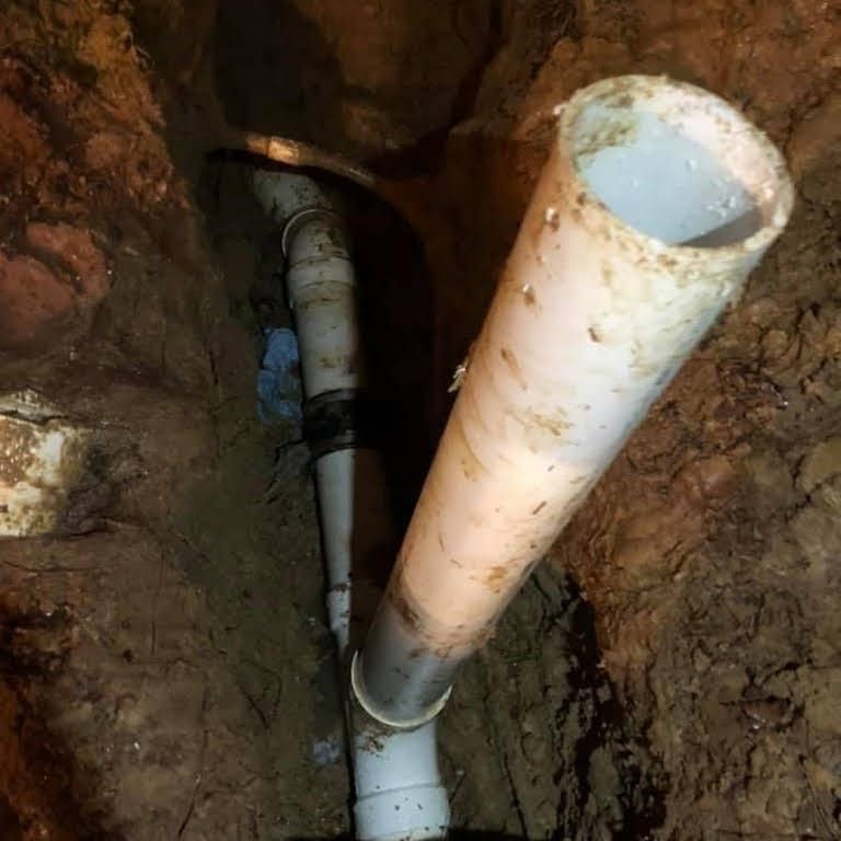 Open trench showing exposed white PVC pipes in dirt, with one pipe angled upward.