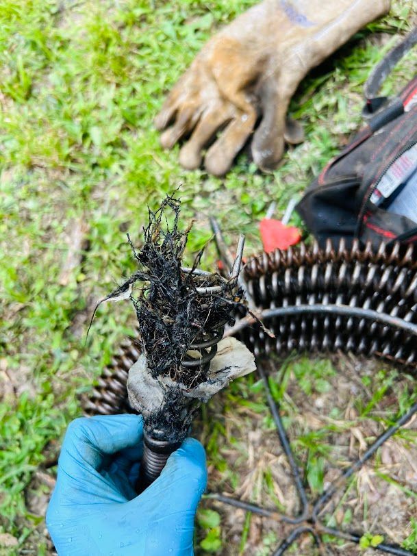 Gloved hand holding a burned cable bundle with exposed wires on grass beside tools and a work glove