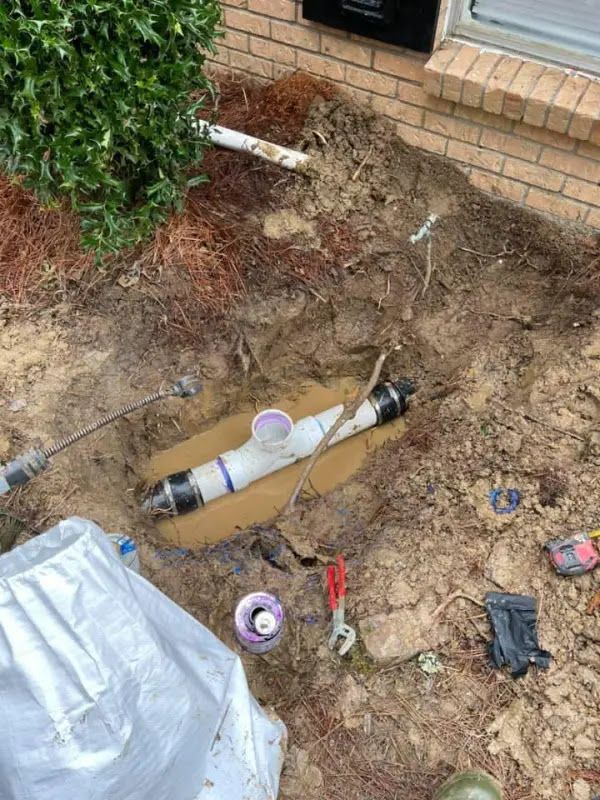 Utility trench with exposed pipe, dirt, and tools beside a brick house step.