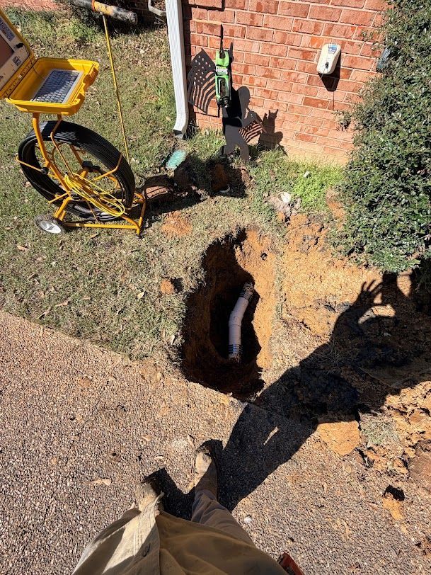 Large sinkhole beside a brick house, with broken ground and a yellow utility cart nearby.