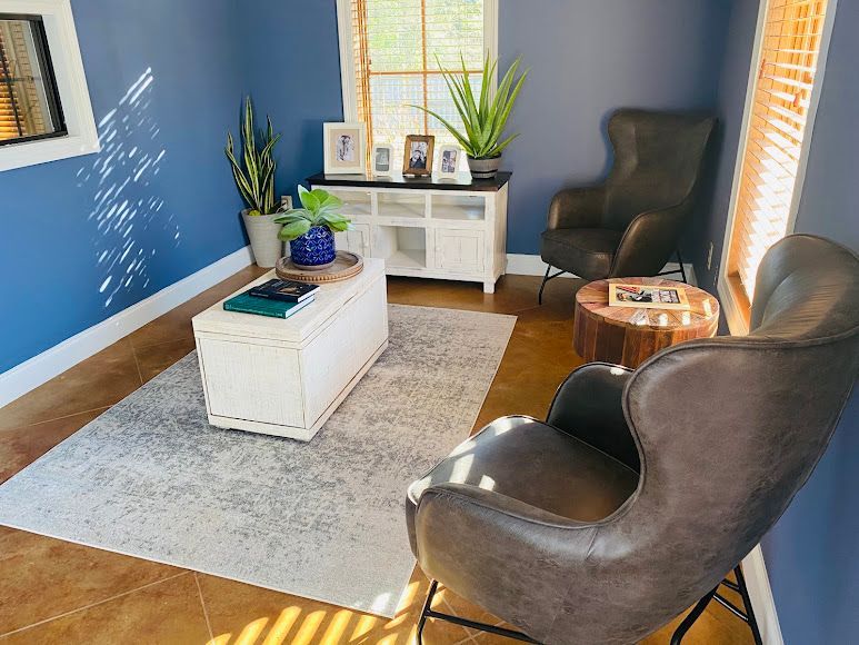 Bright blue living room with two black chairs, white chest coffee table, and small console table by the window.