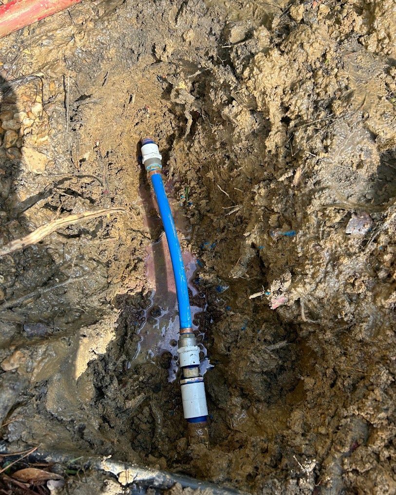 Blue hose connected to a white fitting in a muddy excavation pit.