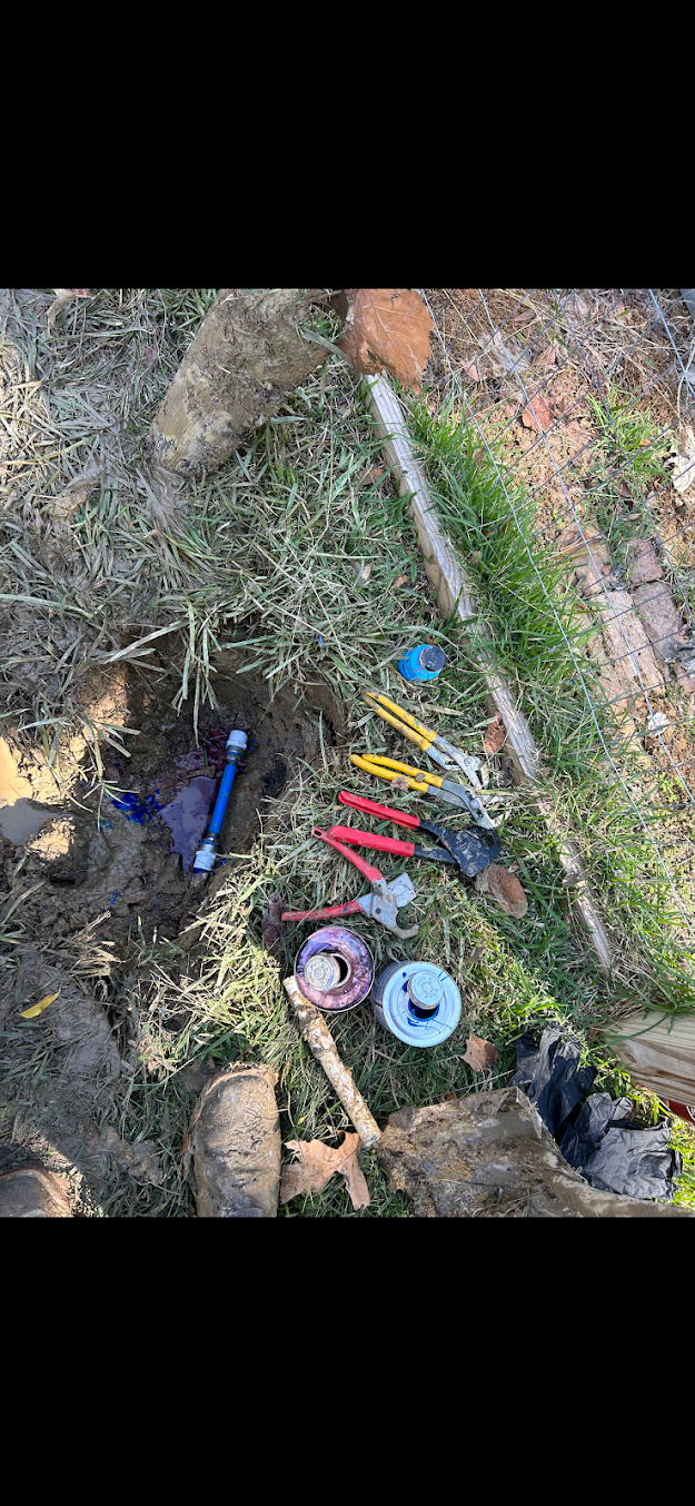 Assorted colorful tools and materials scattered on dirt and grass outdoors near a stone edge.