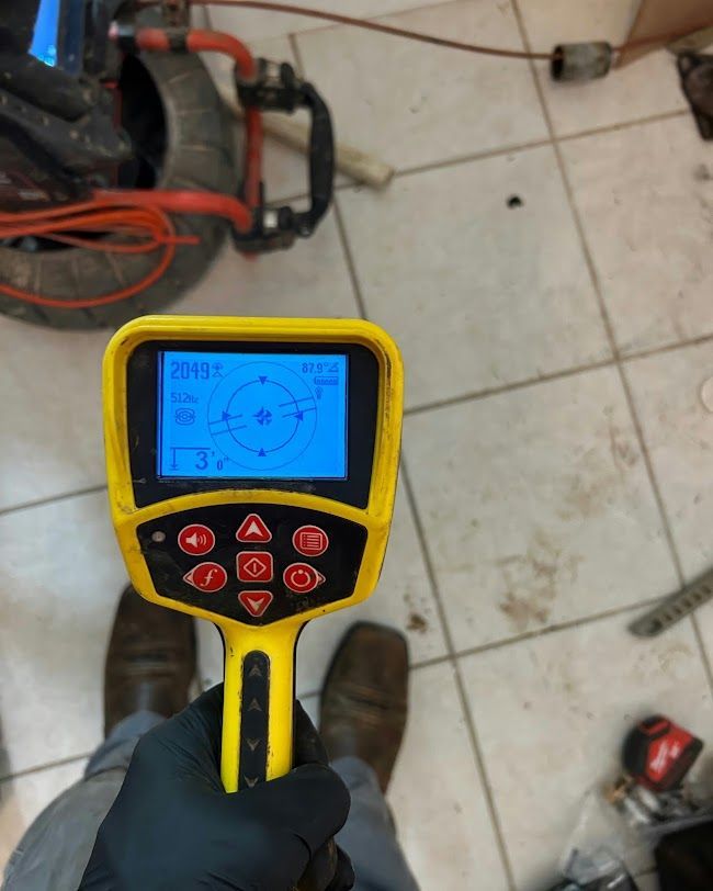 Gloved hand holding a yellow inspection camera device over a tiled floor and red equipment casing