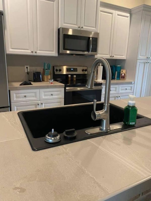 Modern kitchen with white cabinets, black sink, stainless appliances, and beige countertop with green soap bottle
