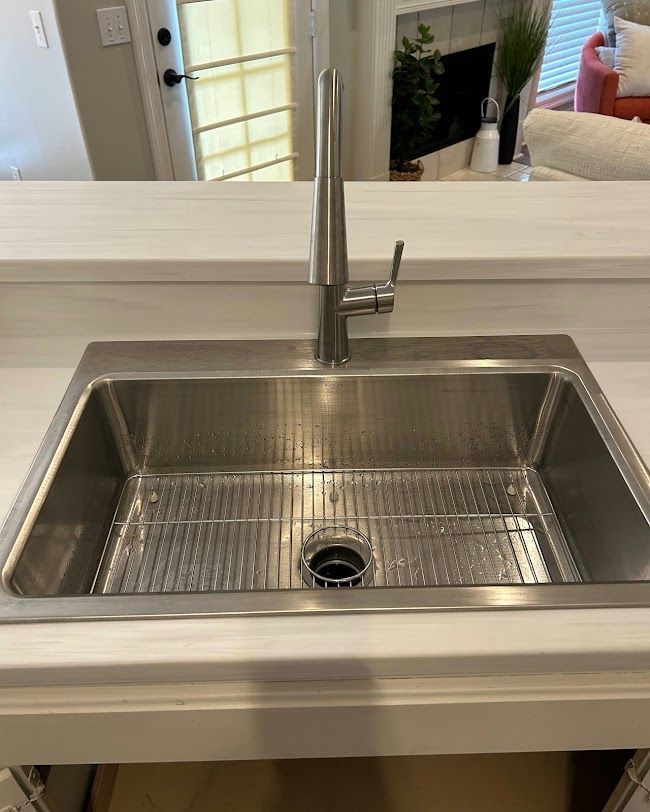 Stainless steel kitchen sink with faucet and white countertop in a bright modern kitchen