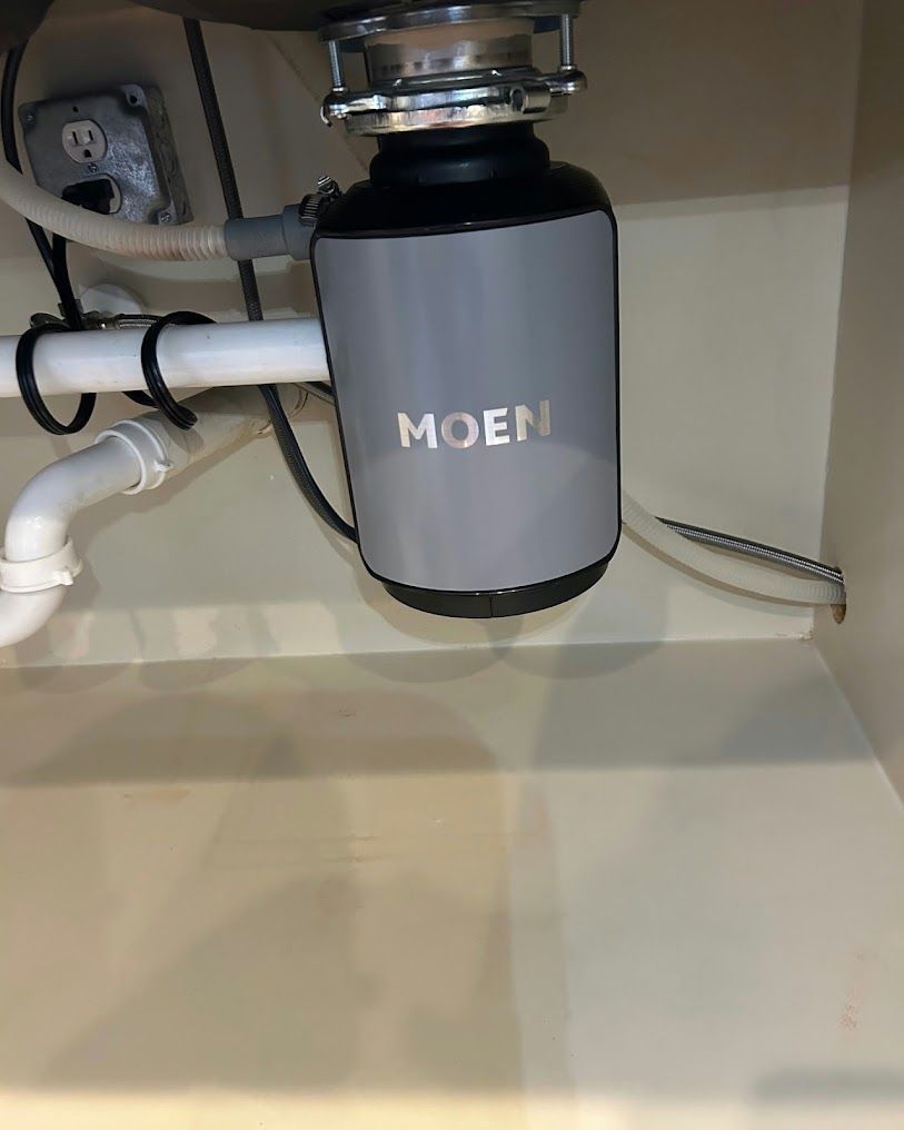 Under-sink disposal unit with gray Moen cover and visible pipes inside a cabinet