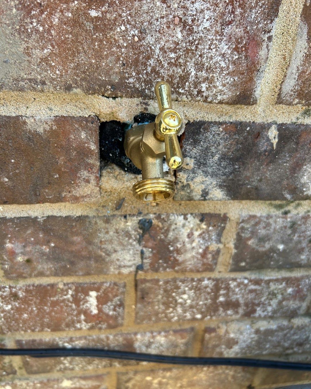 Brass outdoor water spigot mounted on a brick wall with a black cable below
