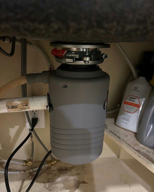 Under-sink garbage disposal with attached plumbing and cleaning supplies on a shelf