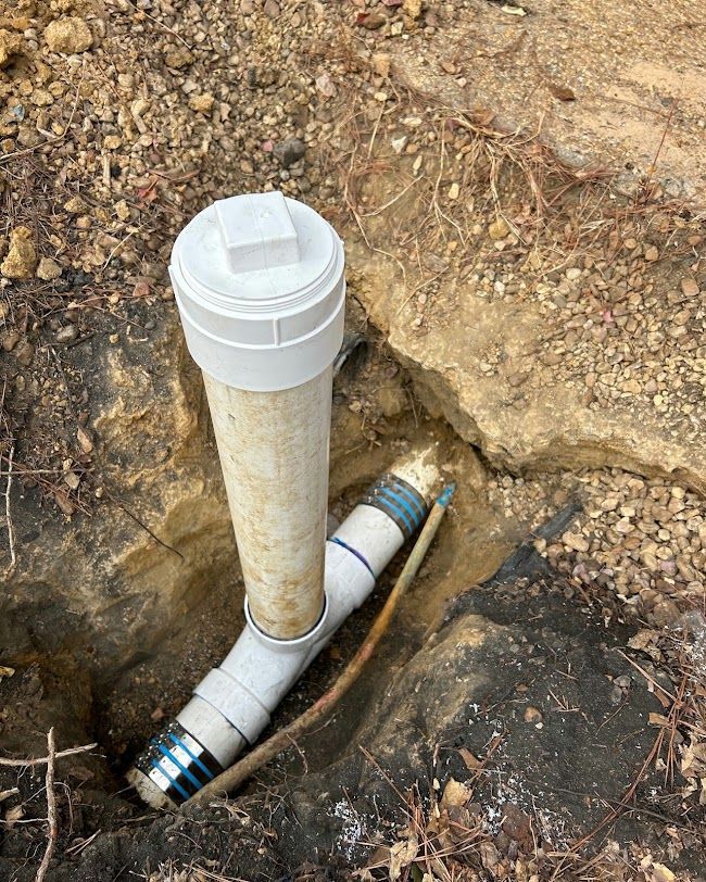 New PVC pipe and capped vent protruding from a dirt trench beside underground plumbing lines