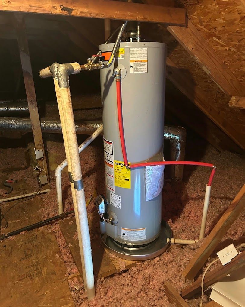 Water heater in an attic with exposed pipes and a red hose connected.