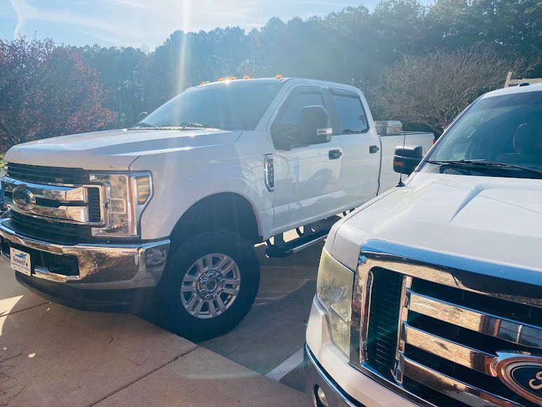 Two white Ford pickup trucks parked side by side in a sunlit lot