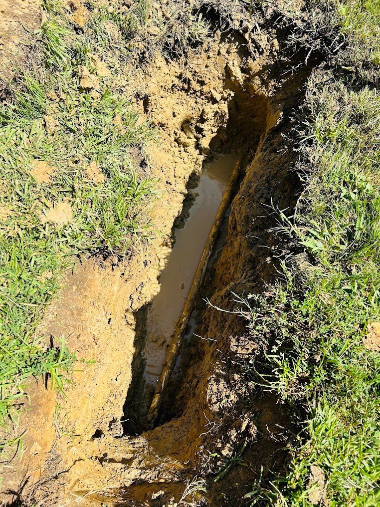 Narrow muddy trench with standing water cutting through grassy soil