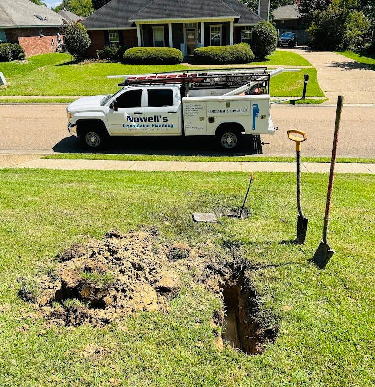 Utility truck parked by a lawn repair trench and dirt pile in a suburban yard.