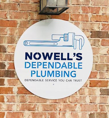 Circular sign for Nowell’s Dependable Plumbing on a brick wall, with blue pipe logo and text.