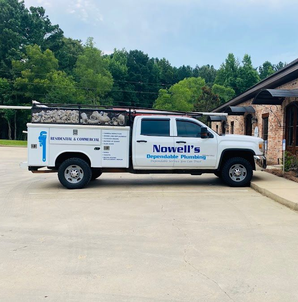 White Nowell's plumbing truck parked outside a brick building under trees