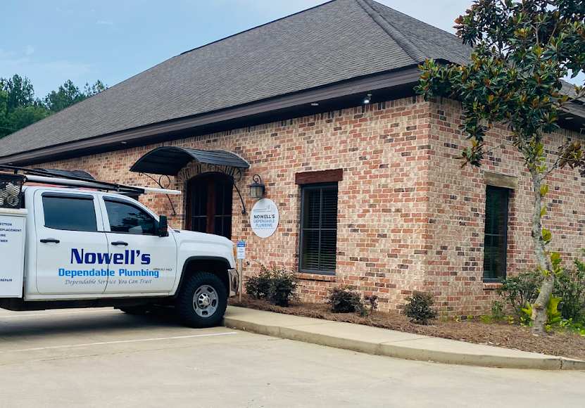 White Novell’s plumbing truck parked beside a brick office building with an arched entrance
