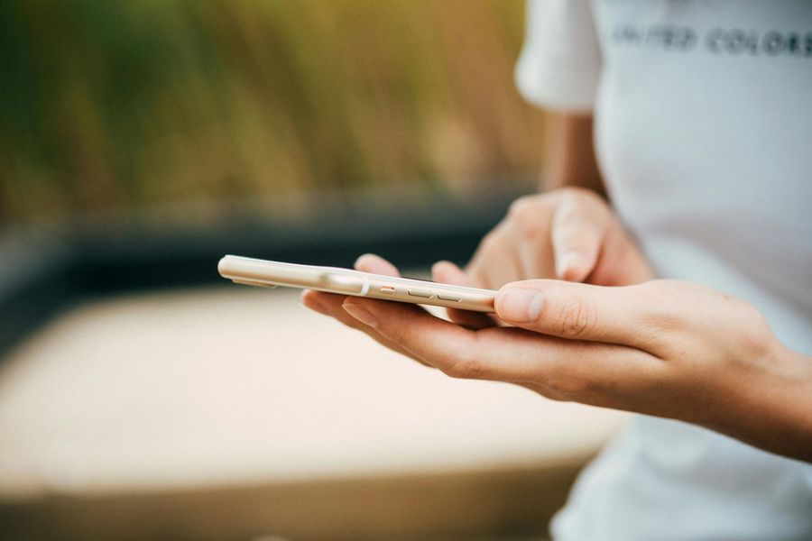 Person holding a smartphone outdoors, using their index finger to tap the screen.