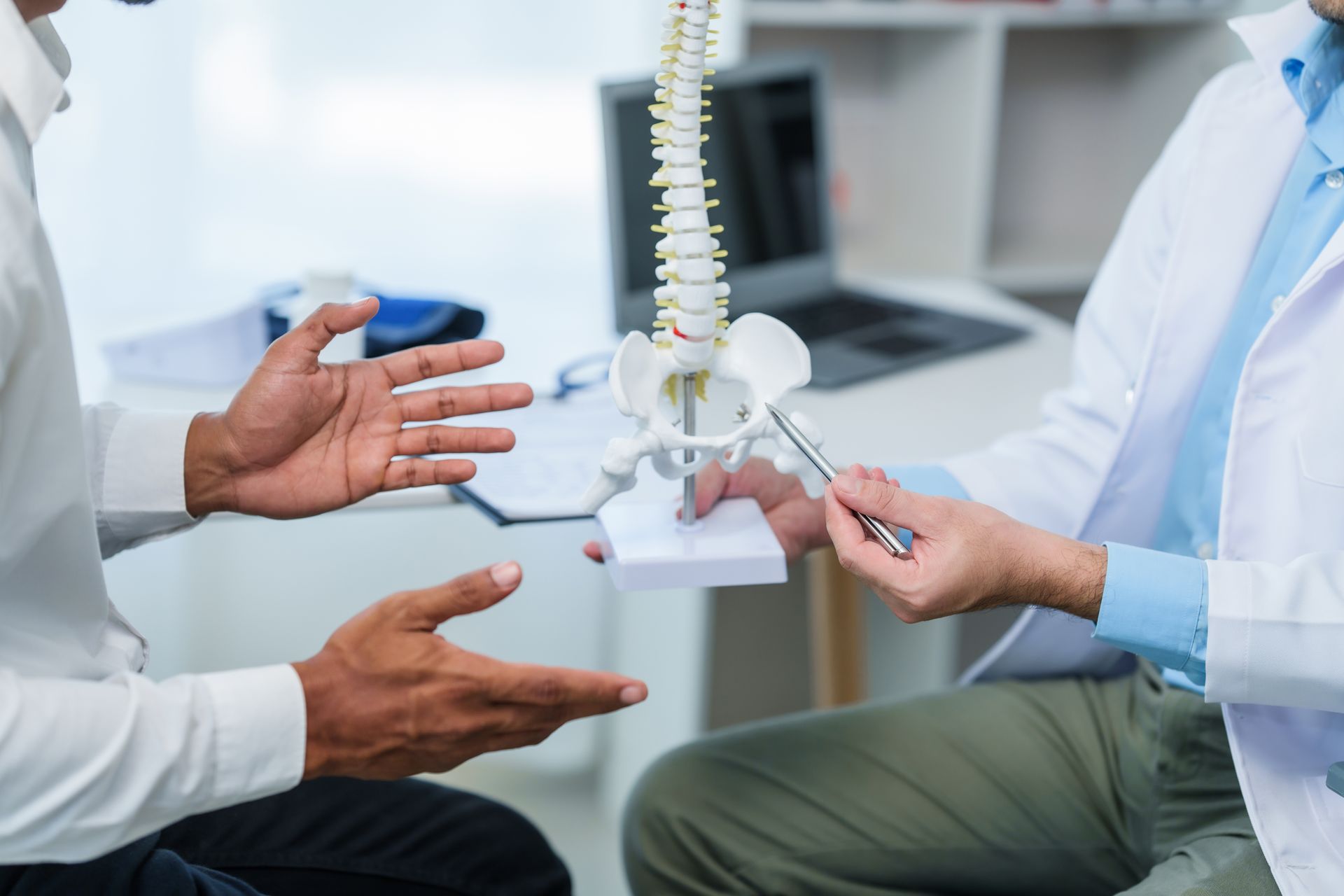 A doctor is holding a model of a spine and talking to a patient.